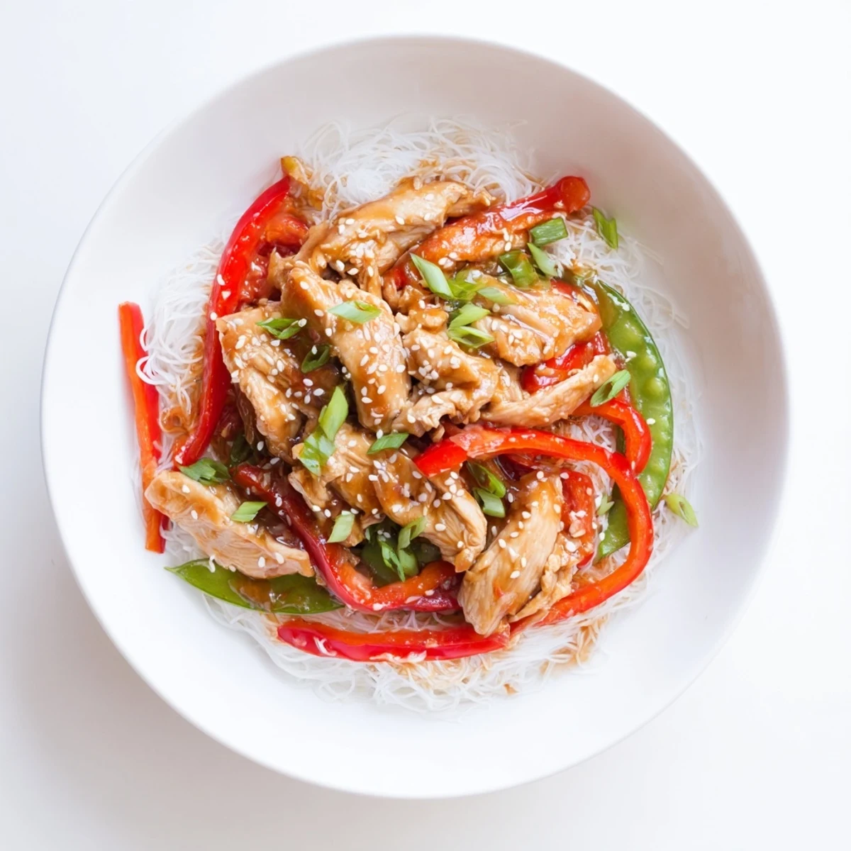 Tender Mongolian Chicken dish with vibrant vegetables and glossy sauce over rice noodles, a delicious meal.