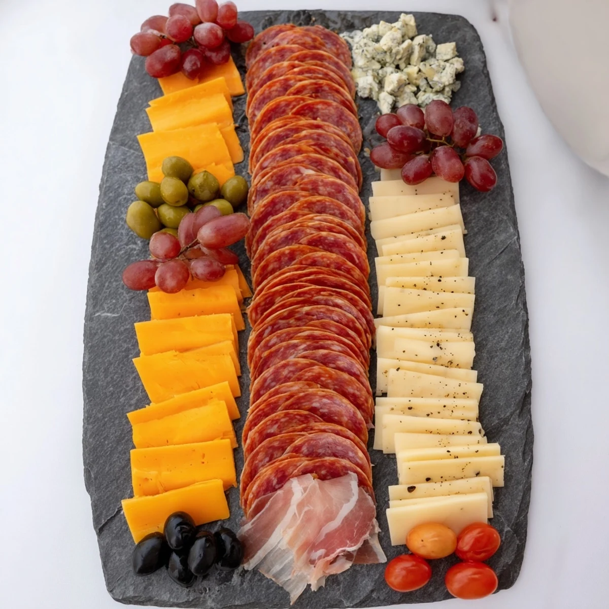 Image of The Industrial Slate appetizer, showcasing meats, cheeses, and grapes on a cold slate.