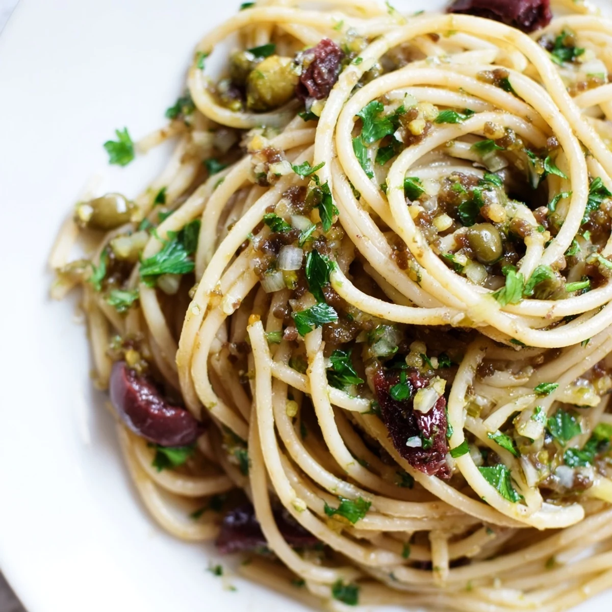 A vibrant bowl of Olive Tapenade Pasta features a rich, briny tapenade coating every strand of al dente spaghetti, garnished with fresh parsley and a bright pop of lemon zest.