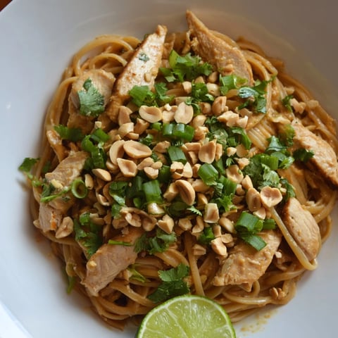 Steaming bowl of Thai Peanut Chicken Pasta, aromatic and garnished with fresh herbs and peanuts.