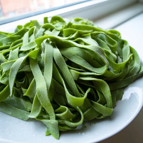 Fresh spinach pasta dough is rolled out on a floured surface, ready for cutting into fettuccine.  