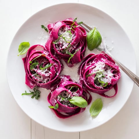 Brightly colored magenta beet noodles tossed in brown butter, garnished with fresh parsley and shaved Parmesan on a rustic plate.  