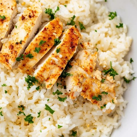 A close-up shows tender chicken breasts over fragrant, buttery rice cooked with sautéed onions and minced garlic.  