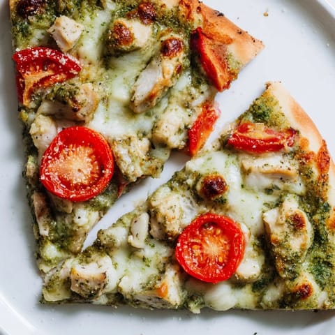 Freshly baked Chicken Pesto Pizza on a wooden board, showing juicy tomatoes and basil leaves garnish for a colorful, aromatic meal.  