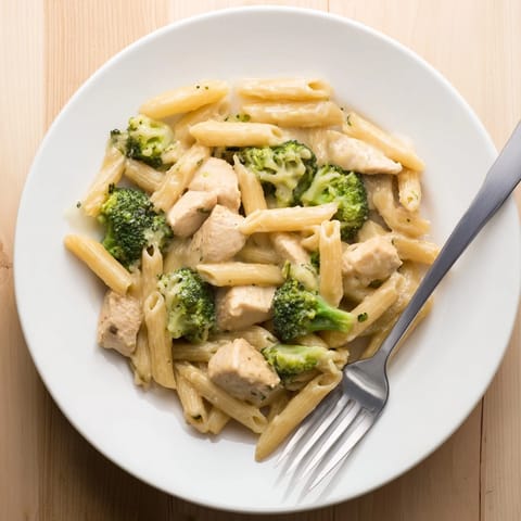 A close-up of creamy Chicken Broccoli Cheddar Pasta on a white plate, penne pasta coated in velvety cheddar sauce with tender chicken and bright green broccoli florets.