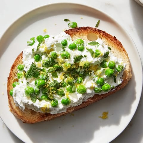 A vibrant plate of pea and mint ricotta toast, garnished with olive oil and black pepper, perfect for brunch.