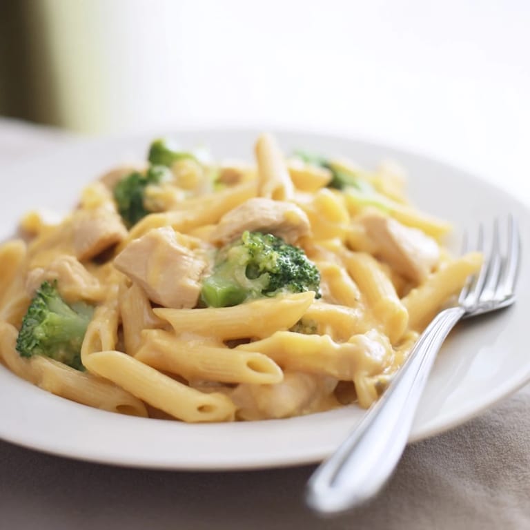 Serving suggestion for family-friendly Chicken Broccoli Cheddar Pasta, garnished with fresh parsley beside a slice of garlic bread on a rustic wooden table.