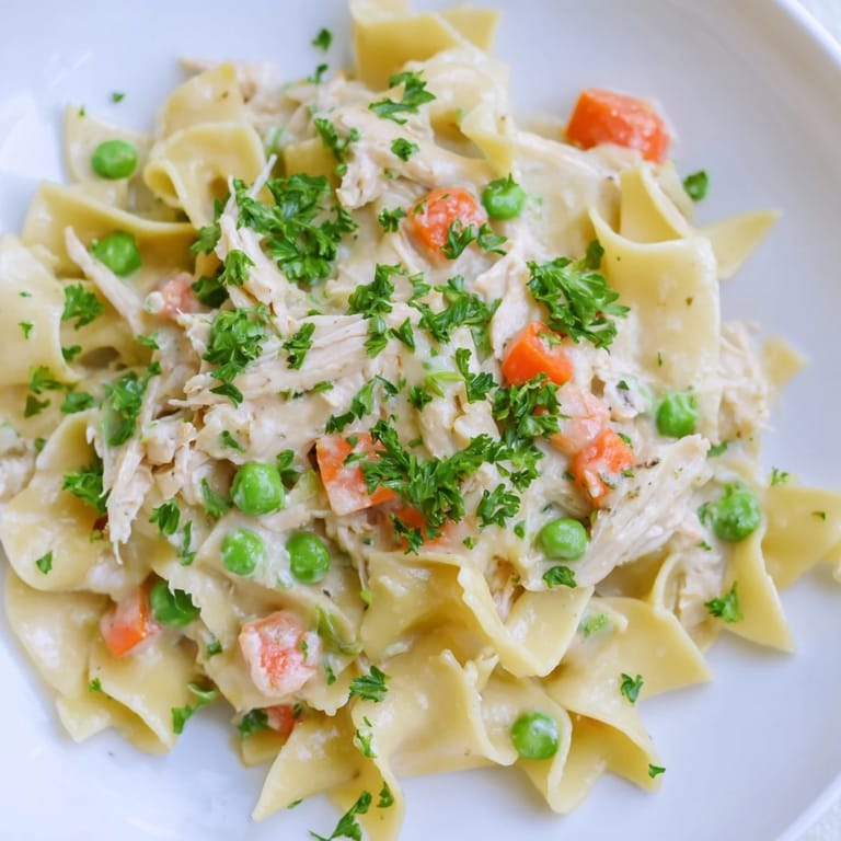 Comforting Spring Chicken Noodle Skillet bubbling in a pan, featuring a light creamy sauce with carrots and peas.